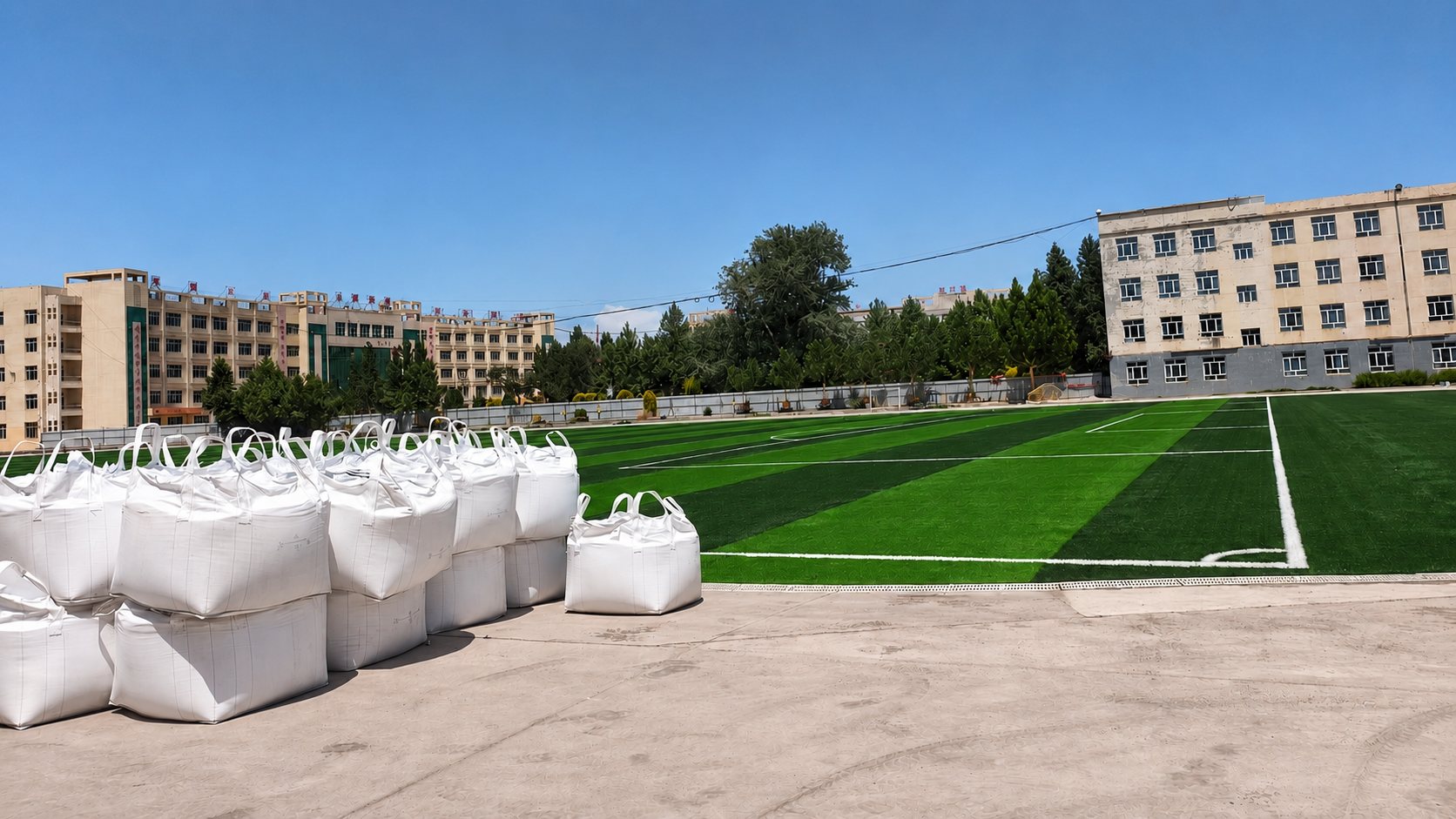 School sports ground with XJ Sports Group material bags staged beside a partly laid artificial turf football field